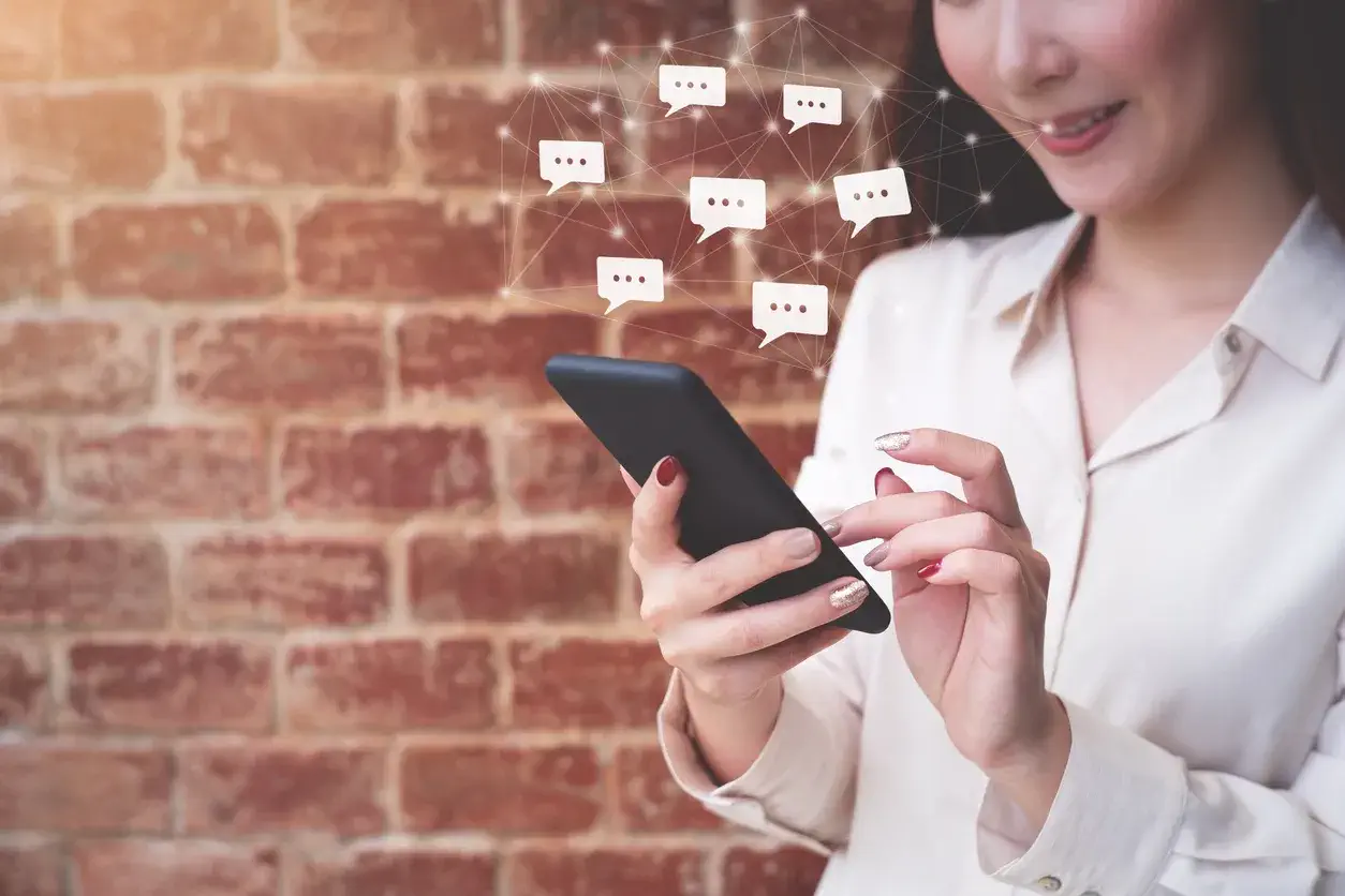 Tuğla duvar önünde akıllı telefon kullanan kadın ve dijital iletişim ikonları.